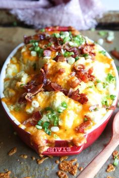 a red bowl filled with macaroni and cheese covered in bacon