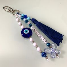 an evil eye keychain with beads and tassels attached to it, on a white surface