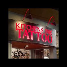 a sign that says kitchen ink tattoo on the side of a building at night time