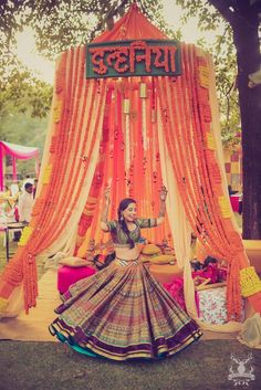 a woman in an orange and blue lehenga sitting on the ground under a canopy