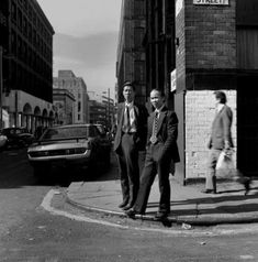 two men in suits are standing on the street corner