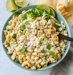 a blue bowl filled with corn salad next to a tortilla shell and lime wedges