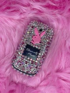 a cell phone with some pink and silver beads on it's back cover, sitting on a furry surface