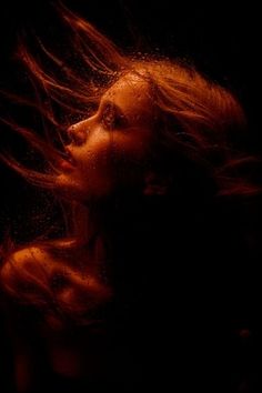 a woman's hair blowing in the wind on a dark background with light coming from her face