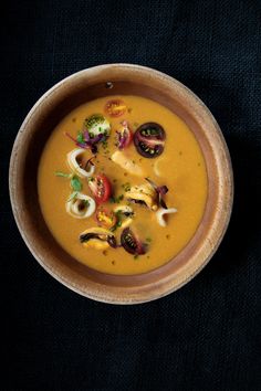 a bowl filled with soup sitting on top of a black cloth covered table next to a spoon