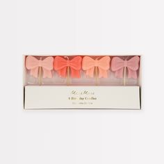 four pink and orange bows are in a white box with gold lettering on the front