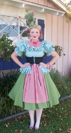 a woman in a dress and hat standing on the grass with her hands on her hips