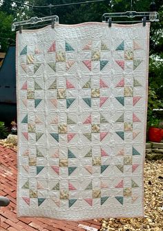 a quilt hanging on a clothes line in front of a brick patio with trees and bushes