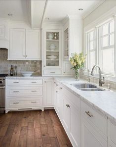 a kitchen with white cabinets and wood floors is pictured in this image, there are flowers on the window sill