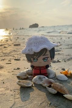 a stuffed doll sitting on top of a sandy beach next to the ocean with seashells