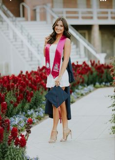 a woman wearing a pink sash standing in front of red and blue flowers with her hand on her shoulder