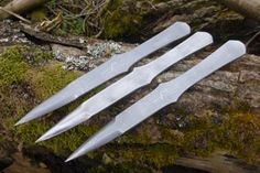 three knives laying on top of a moss covered log