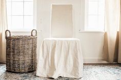 a white chair sitting in front of a window next to a basket on the floor