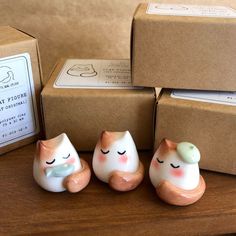 three small ceramic cats sitting next to each other on a wooden table in front of boxes