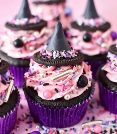 some cupcakes with pink frosting and black hats on top are surrounded by sprinkles