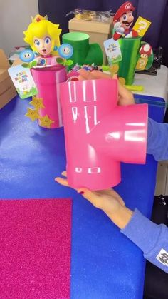 a person holding up a pink cup with mario and luigi on it at a table