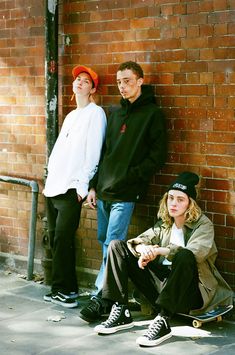 three young men are leaning against a brick wall