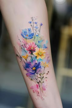 a watercolor style flower tattoo on the left arm and leg, with colorful flowers painted all over it