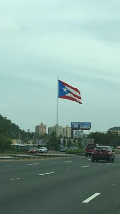 an american flag flying on the side of a highway next to a freeway with cars driving down it