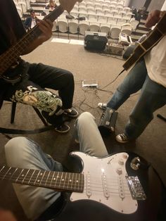 two men are playing guitars in an empty room with rows of chairs and seats behind them