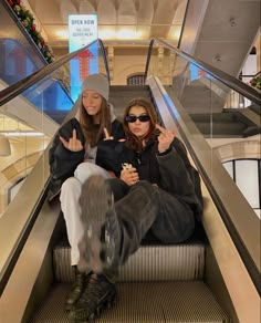 two women sitting on an escalator with their hands in the air and pointing