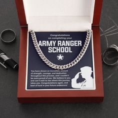 an army ranger school necklace is displayed in a red box with silver chains on it