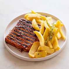 a white plate topped with grilled meat and french fries on top of a table