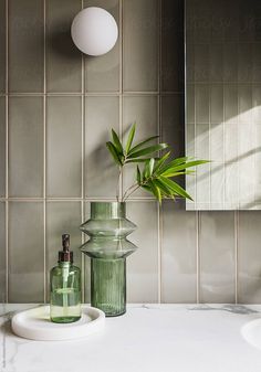 a green vase sitting on top of a counter next to a mirror and soap dispenser