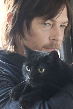 a man holding a black cat in his arms and looking at the camera with an intense look on his face