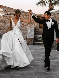 a man and woman in formal wear walking down the street with their hands in the air