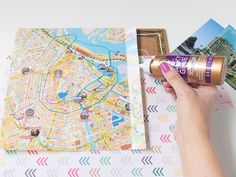 a hand holding a can of beer next to a map and postcard with the city on it