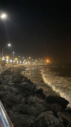 an empty street next to the ocean at night with lights on and people walking along it