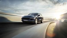 a black porsche cayen driving down the road at sunset or dawn with clouds in the background