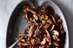 a bowl filled with meat and mushrooms on top of a metal table next to a spoon