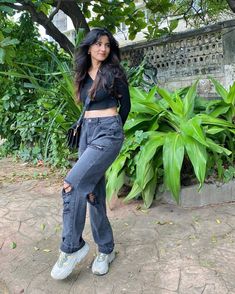 a woman standing in front of some plants and trees with her leg up on the ground