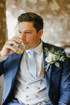 a man in a suit and tie drinking from a glass while sitting on a chair