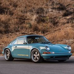 a blue porsche sits parked on the side of the road in front of some brown grass