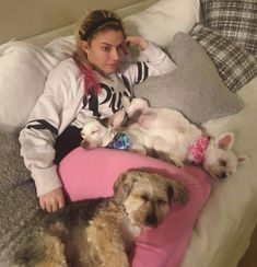 a woman laying on top of a bed next to two small white and brown dogs