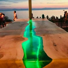 people are standing on the edge of a dock with water running down it and green lights reflecting in the water