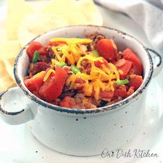 a bowl filled with chili and cheese on top of a white plate next to tortilla chips