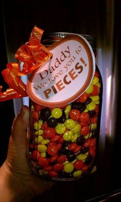 a person holding up a jar filled with candy and candies that says daddy we love you pieces