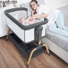 a woman laying in bed next to a baby with a crib on the floor