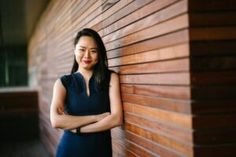 a woman standing next to a wooden wall with her arms crossed and looking at the camera