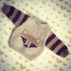 a knitted sweater with a raccoon on it laying on top of a bed