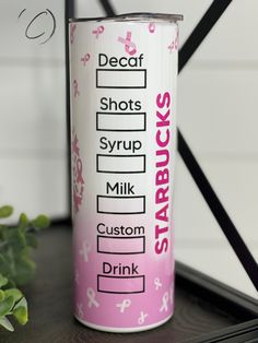 a pink and white coffee cup sitting on top of a table next to a plant