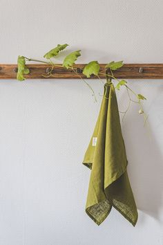 two green napkins hanging from a wooden rack next to a white wall and plant