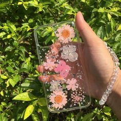 a hand holding up a clear case with flowers on the front and back cover, in front of some bushes