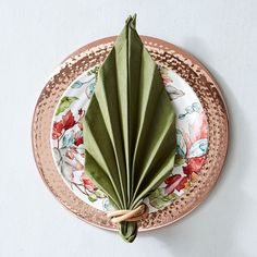 a folded green leaf sitting on top of a white and gold plate with pink flowers