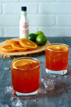 two glasses filled with orange juice next to some limes