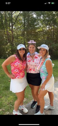 three women standing next to each other in front of some trees and grass with their arms around one another